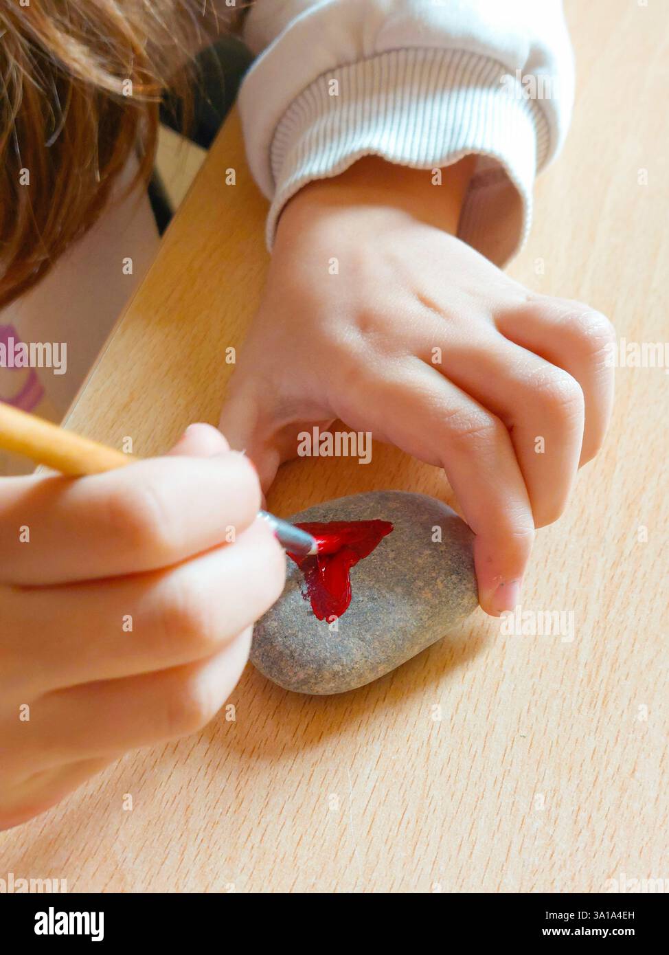 Enfant s'amusant avec l'activité créative, peindre la forme de coeur rouge sur la roche à l'aide d'un pinceau Banque D'Images