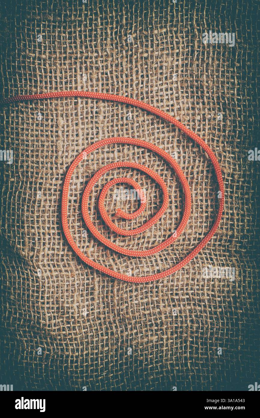 Filet en spirale rouge sur fond jute. Image abstraite et verticale idéale pour une couverture de livre. Banque D'Images