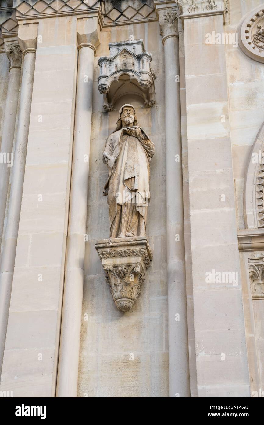 Élégante statue en pierre d'une figure religieuse ornant la façade d'une ancienne cathédrale européenne pendant l'heure dorée du coucher du soleil Banque D'Images