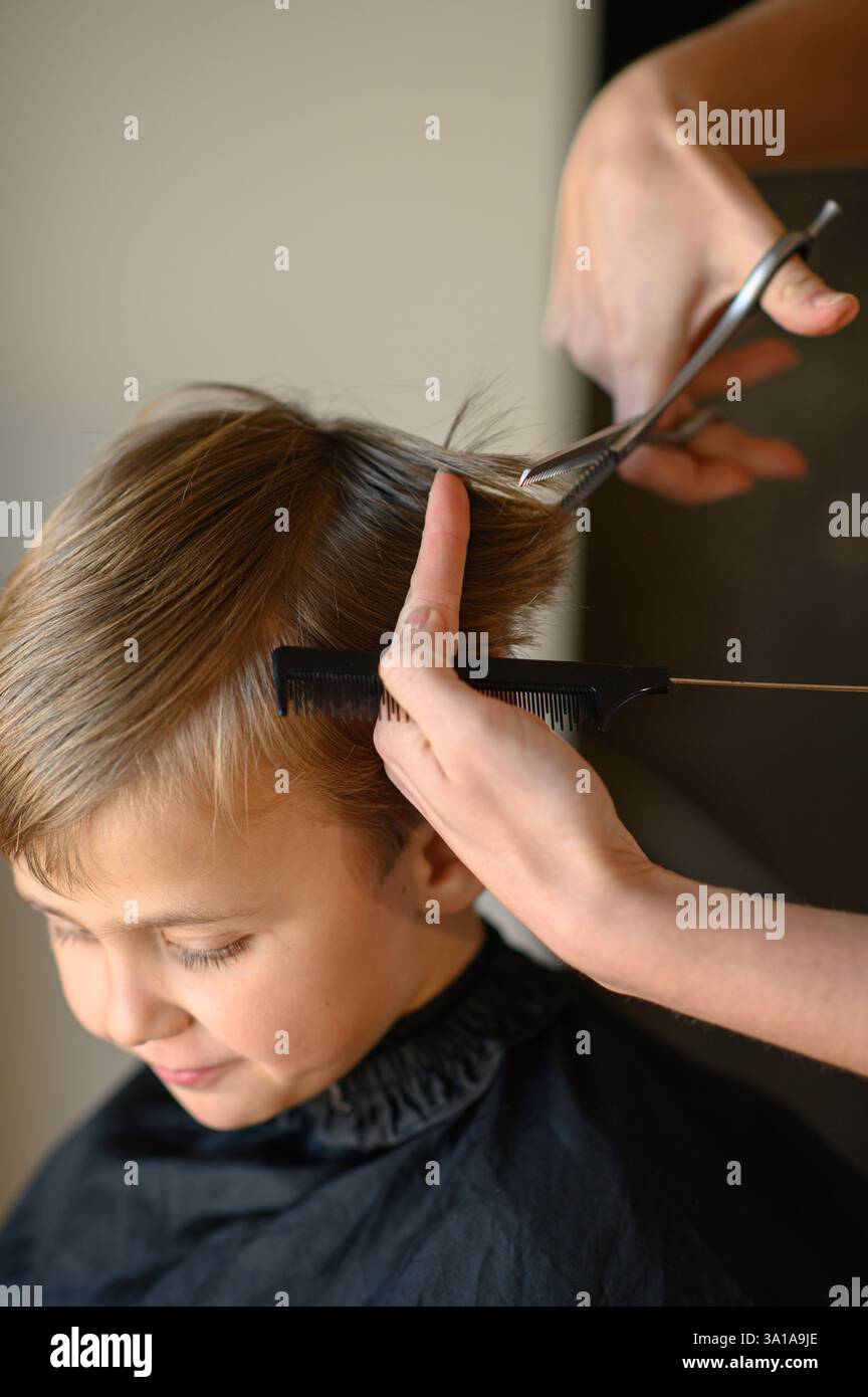 Le coiffeur amincit les cheveux du garçon avec des ciseaux amincissants. Banque D'Images