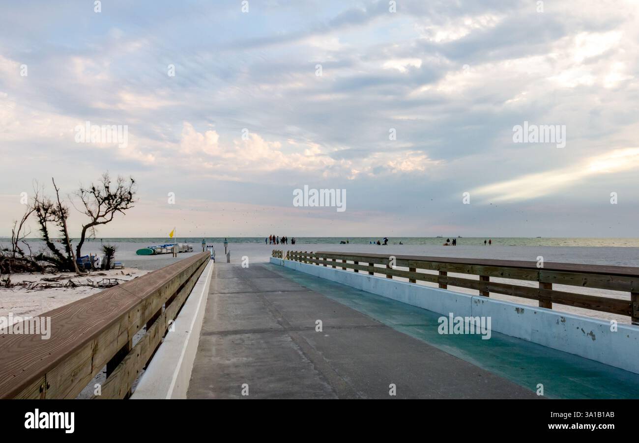 19/02/2025, Fort Myers, FL, États-Unis – Un pont panoramique menant à Lovers Key Beach, entouré de sable et de verdure. Le ciel bleu vif avec des nuages sinueux met en valeur Banque D'Images