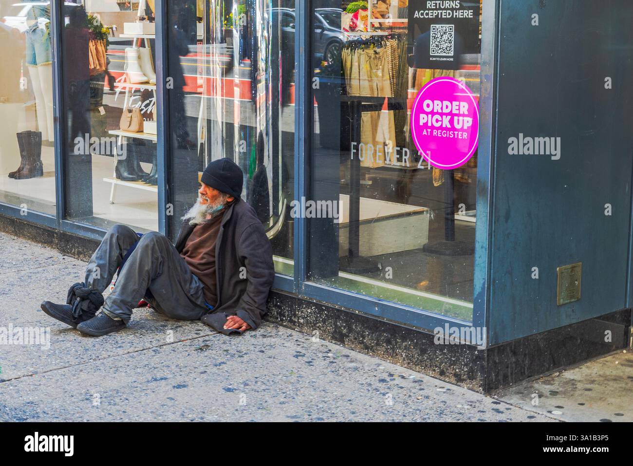 Mendiant sans abri assis sur le trottoir près de l'entrée du magasin tandis que les piétons passent sur la 34e rue à New York. New York. ÉTATS-UNIS Banque D'Images