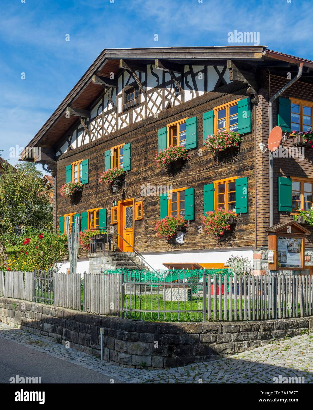 Rettenberg, Gästehaus Stork, vieille maison en bois avec pignon à colombages, fleurs devant les fenêtres et volets verts. Banque D'Images