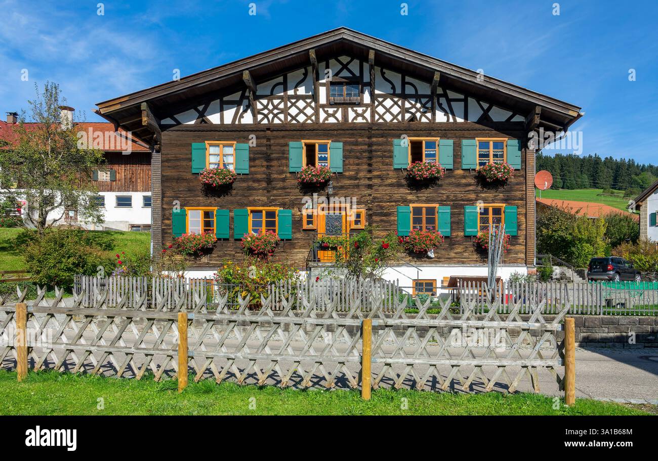 Rettenberg, Gästehaus Stork, vieille maison en bois avec pignon à colombages, fleurs devant les fenêtres et volets verts. Banque D'Images