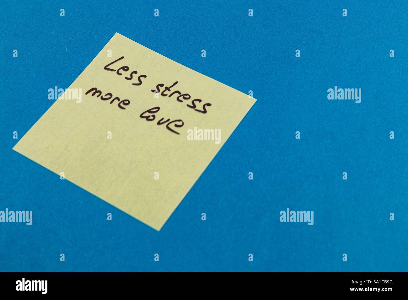 Une note collante avec le message moins de stress plus d'amour se trouve sur une surface bleue vibrante, encourageant la positivité et favorisant un changement d'état d'esprit vers le bien Banque D'Images