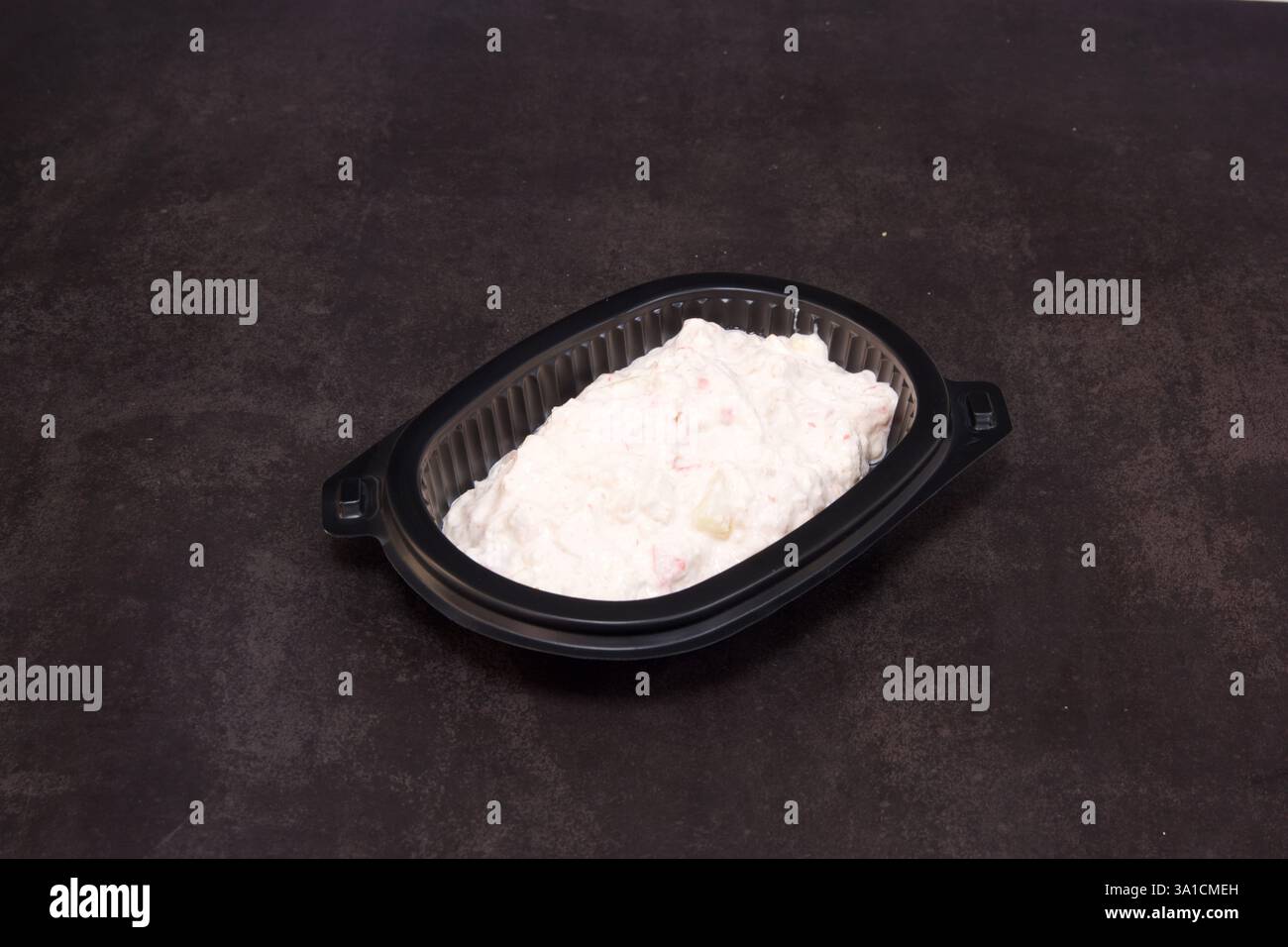 Un petit récipient en plastique avec une substance blanche dedans. Le récipient est noir et repose sur une surface sombre Banque D'Images