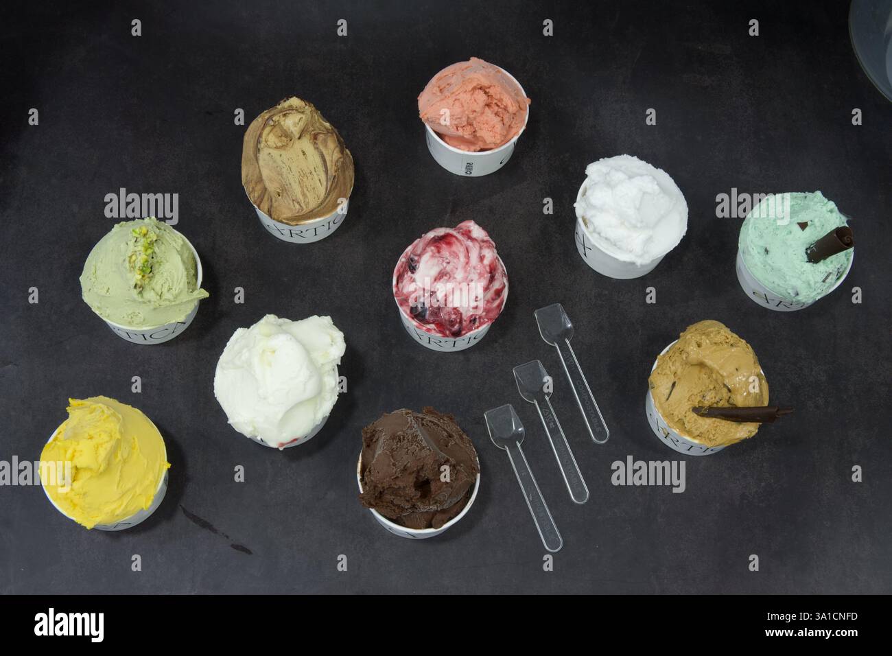 Une rangée de tasses de crème glacée avec différentes saveurs, y compris le chocolat, la fraise et la vanille. Les tasses sont disposées en une rangée nette sur une table Banque D'Images