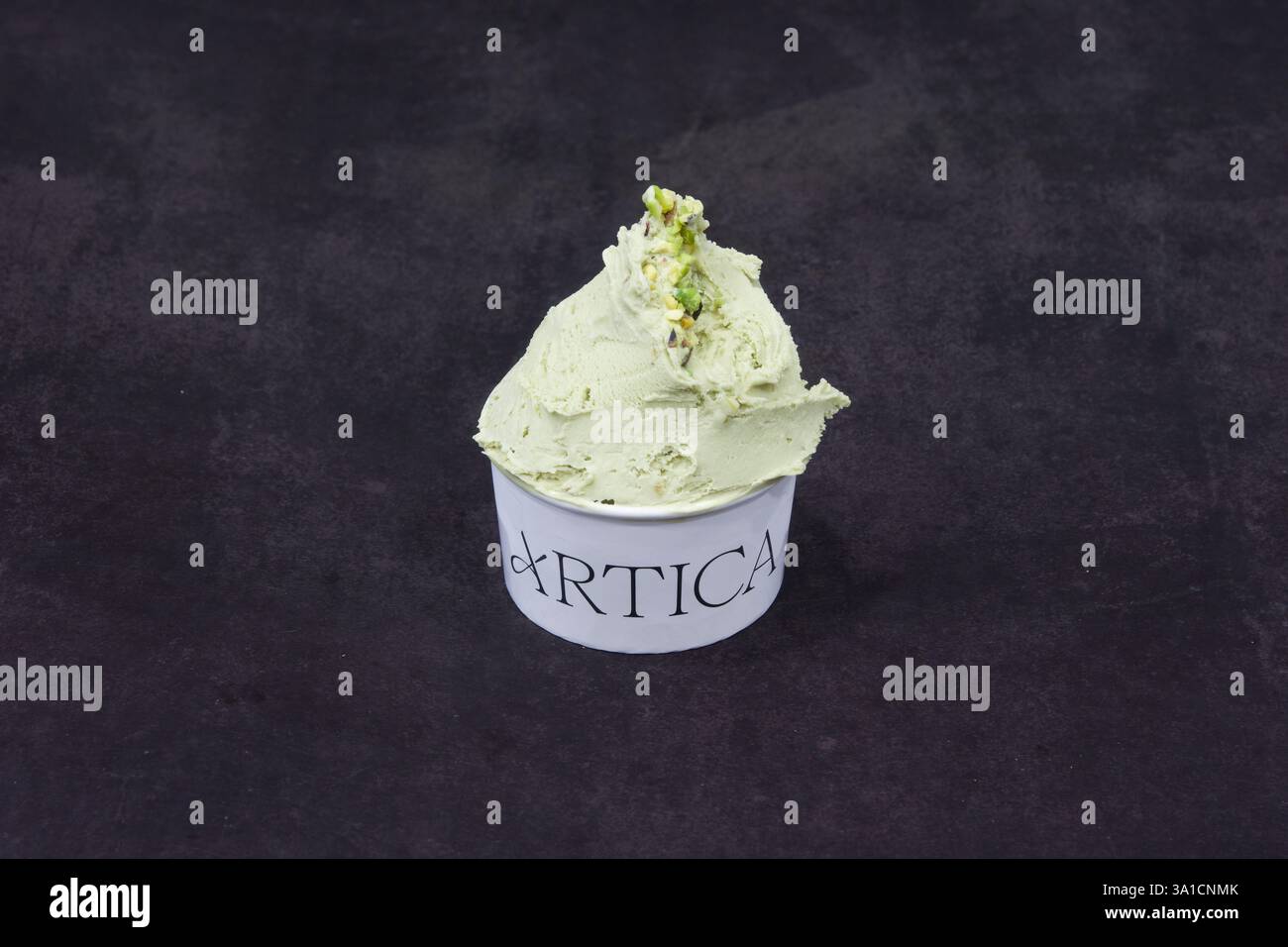 Une boule de crème glacée verte dans une tasse blanche avec le mot Artica écrit dessus. La crème glacée repose sur une surface noire Banque D'Images