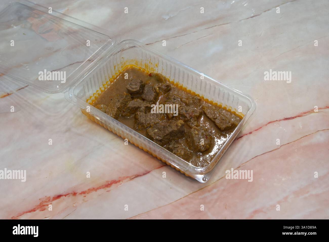 Un récipient de viande avec sauce sur un comptoir en marbre. Le récipient est en plastique et a un couvercle Banque D'Images