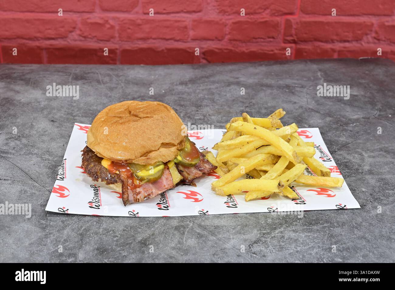 Un hamburger et des frites sur une assiette en papier. Le hamburger est garni de cornichons et de moutarde. Les frites sont dorées et croustillantes Banque D'Images