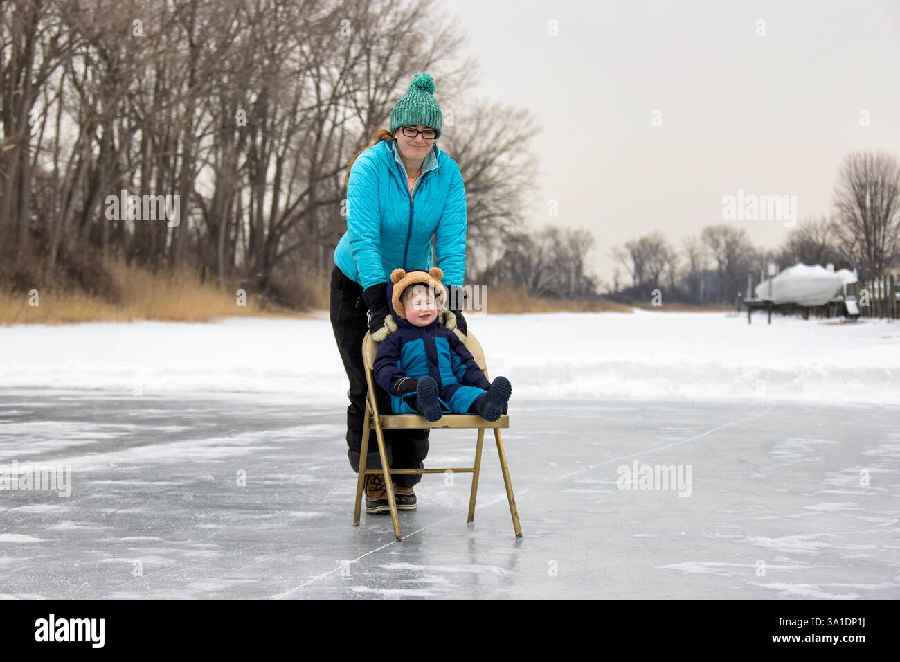 Femme poussant son enfant dans une chaise sur un étang gelé en hiver. Banque D'Images