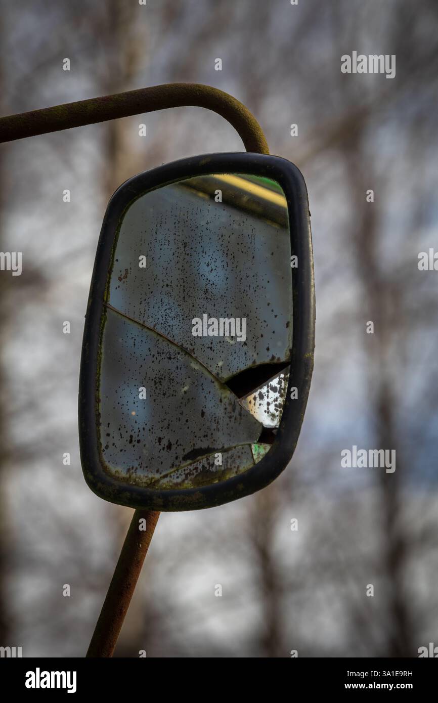 Gros plan d'un miroir de tracteur fissuré et sale reflétant des branches d'arbre qui se fondent avec l'arrière-plan Banque D'Images