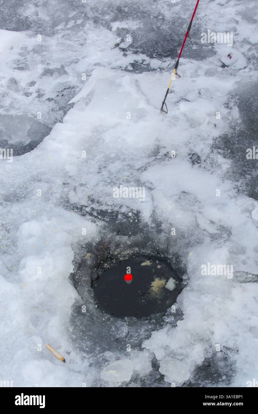 C'est une photo descendante d'un trou de pêche sous glace. Le trou est une ouverture sombre et à peu près circulaire dans la surface gelée, probablement un lac. Banque D'Images