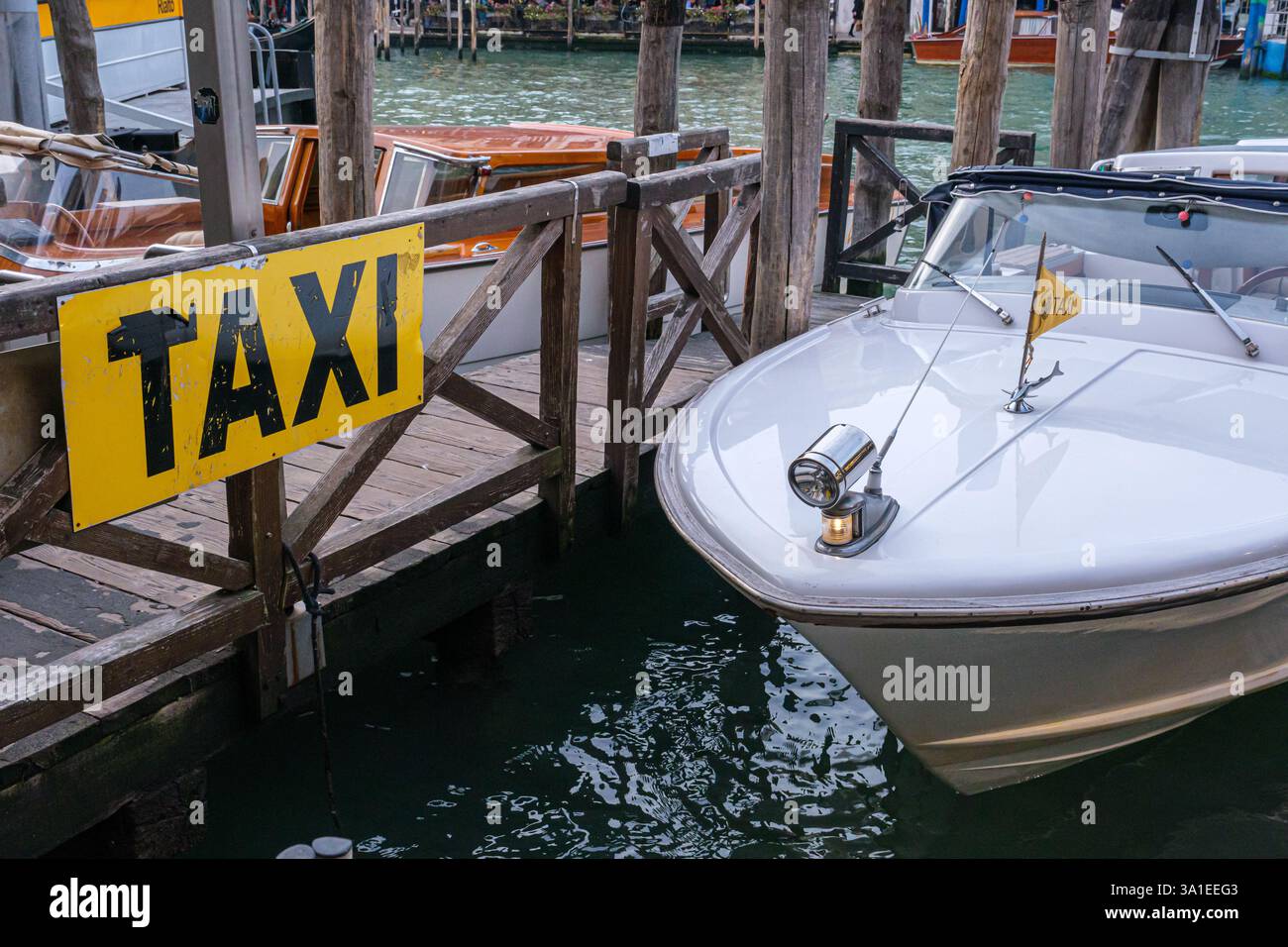 Venise, Italie - 12 octobre 2024 : un taxi d'eau vive amarré à un quai en bois avec un panneau jaune pour les taxis Banque D'Images