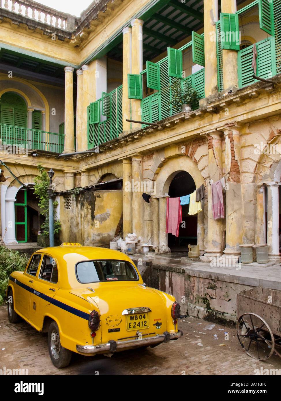 Un taxi Ambassador jaune stationné dans la cour d'un ancien bâtiment Kolkata à l'architecture coloniale et aux volets en bois vert. Banque D'Images