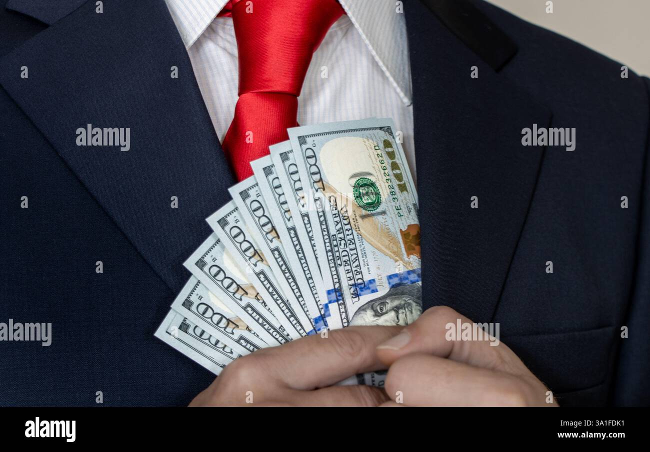 Un homme riche en costume et cravate compte les dollars américains dans sa main et les met dans sa poche. Gagner de l'argent, homme d'affaires prospère, investisseur Banque D'Images
