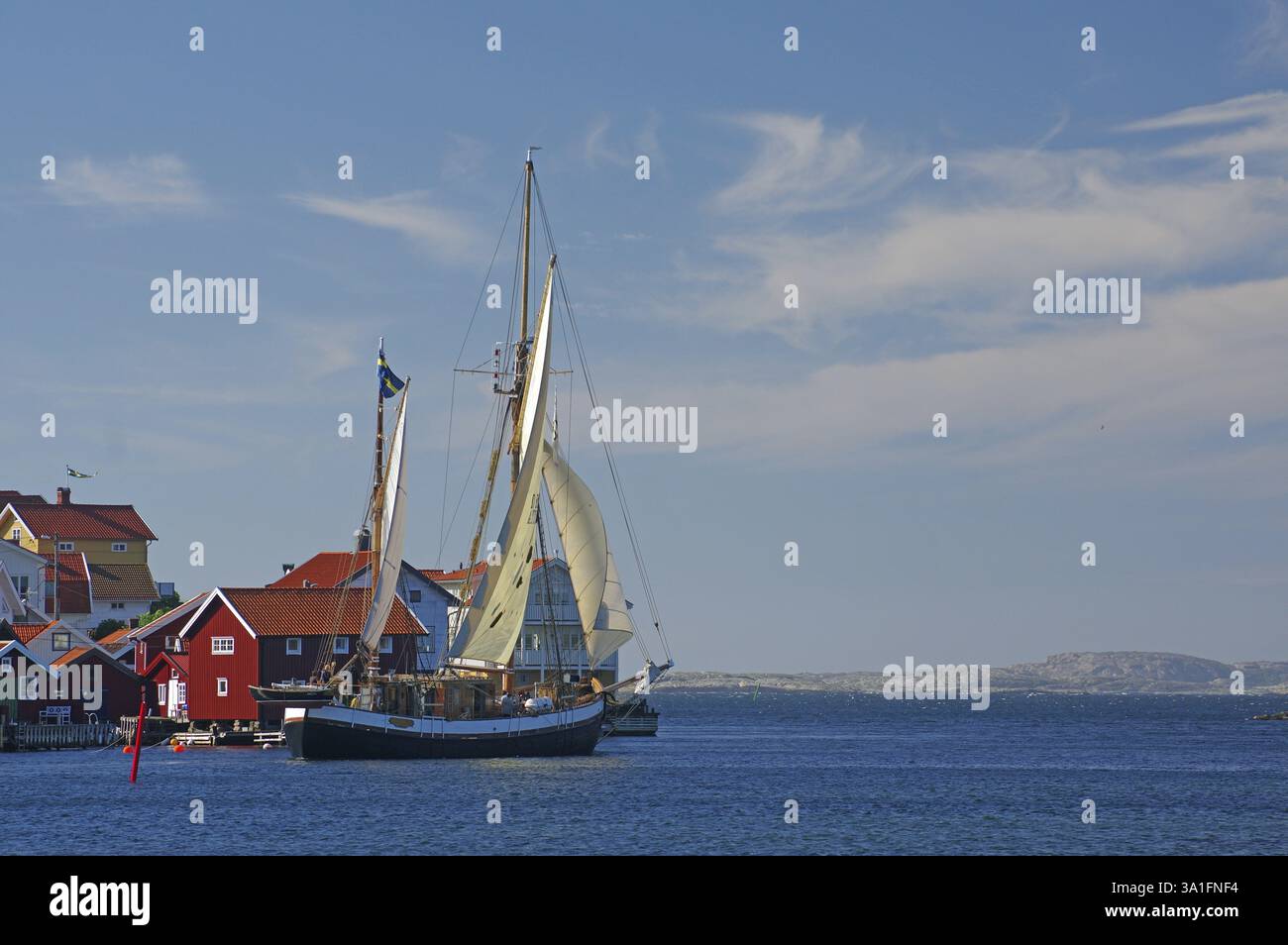 Bateau à voile historique dans le port à côté de maisons colorées, vent léger dans la voile, ciel bleu avec des nuages, Gullholmen, Vaestra Goetalands laen, Swed Banque D'Images