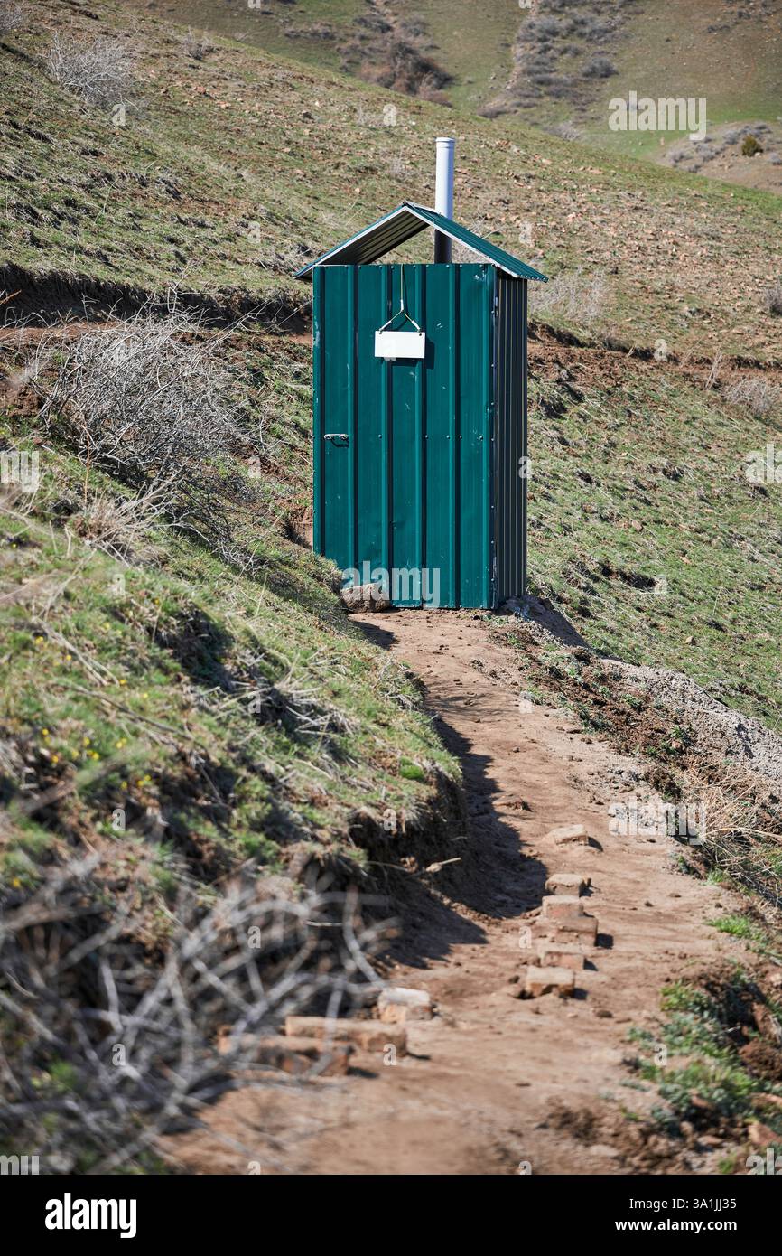 chemin vers la structure de toilettes extérieures en feuilles ondulées vertes. Cabine de toilette avec un signe blanc vide. Banque D'Images
