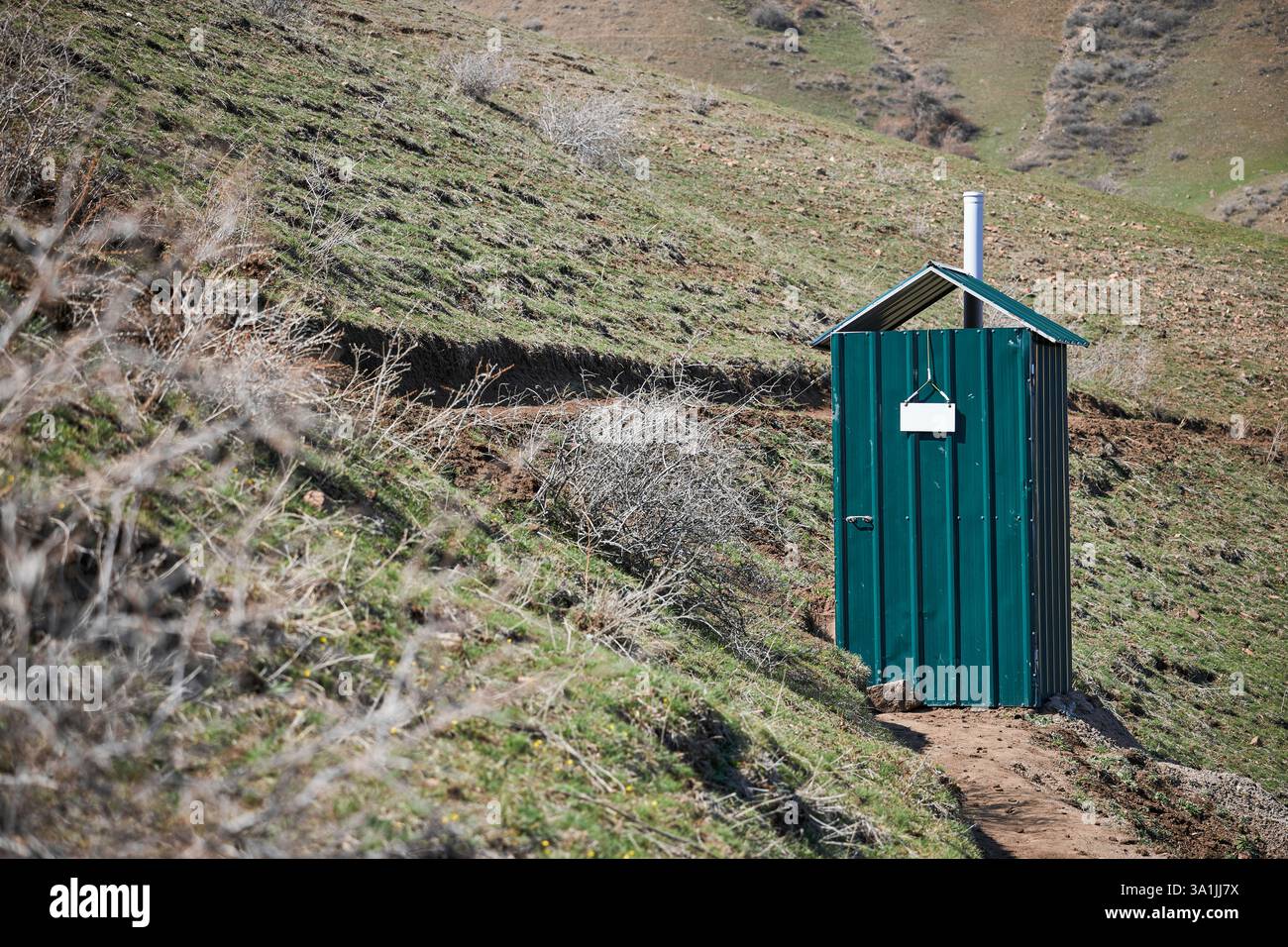 Structure de toilettes extérieures de campagne en feuilles ondulées vertes. Cabine de toilette avec un signe blanc vide. Banque D'Images