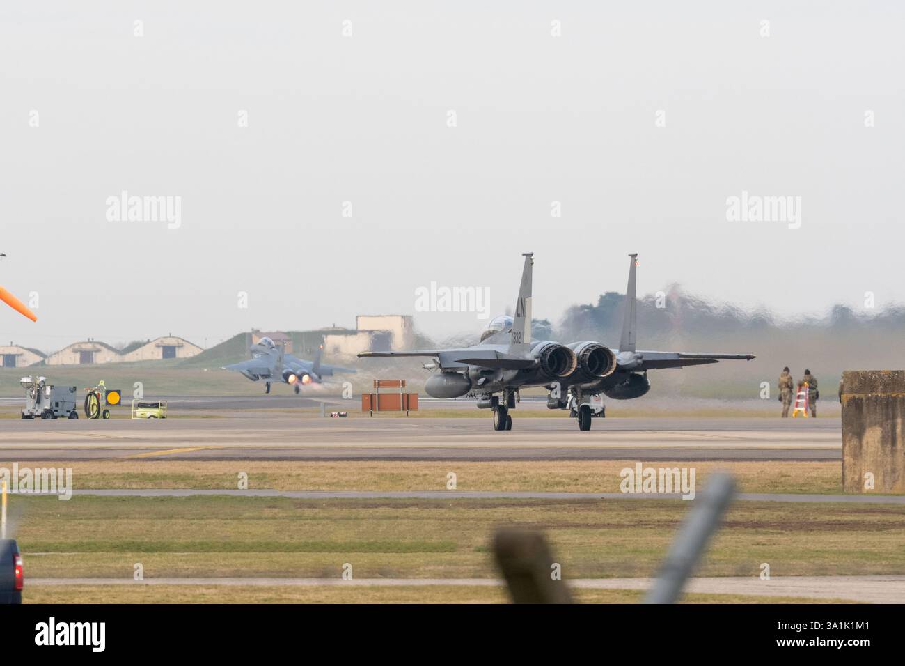 USAF McDonnell Douglas F-15 Eagle regarde un autre F-15 de l'USAF quitter RAF Lakenheath, Suffolk avec réchauffage / postcombustion. L'équipe au sol surveille également. Banque D'Images