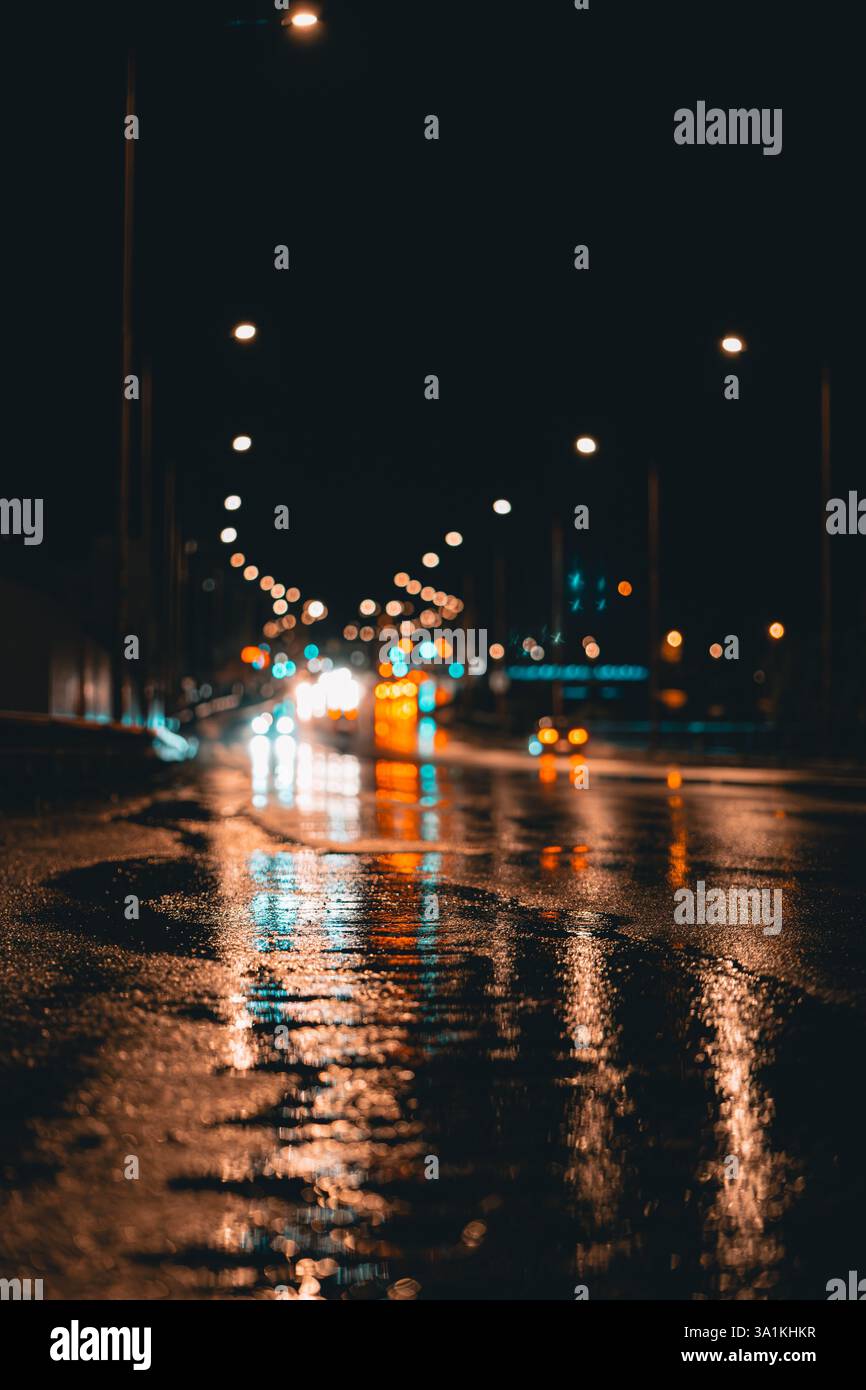 Route de nuit pluvieuse avec lumières de voiture reflétant sur asphalte humide Banque D'Images