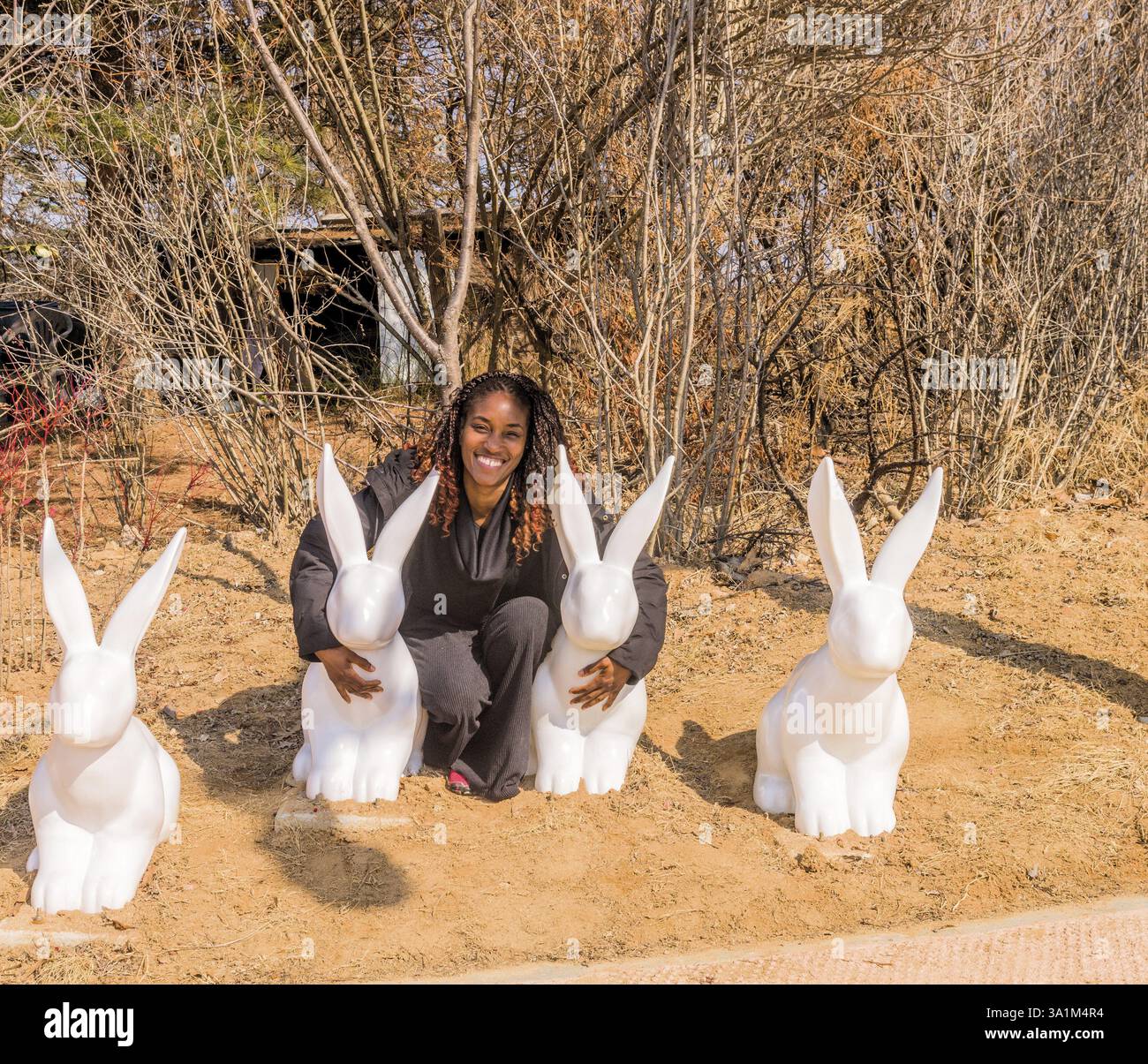 Jeune femme noire embrassant de grandes statues de lapin blanc dans un cadre de parc. Prise à Daejeon, Corée du Sud, Asie Banque D'Images