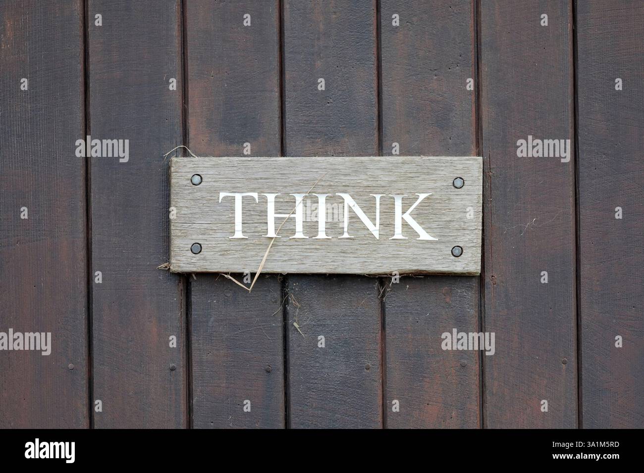 Un panneau en bois indiquant « PENSER » en lettres majuscules blanches sur un fond Uni, fixé à une porte en bois brun avec des planches verticales à l'aide de quatre vis. Banque D'Images
