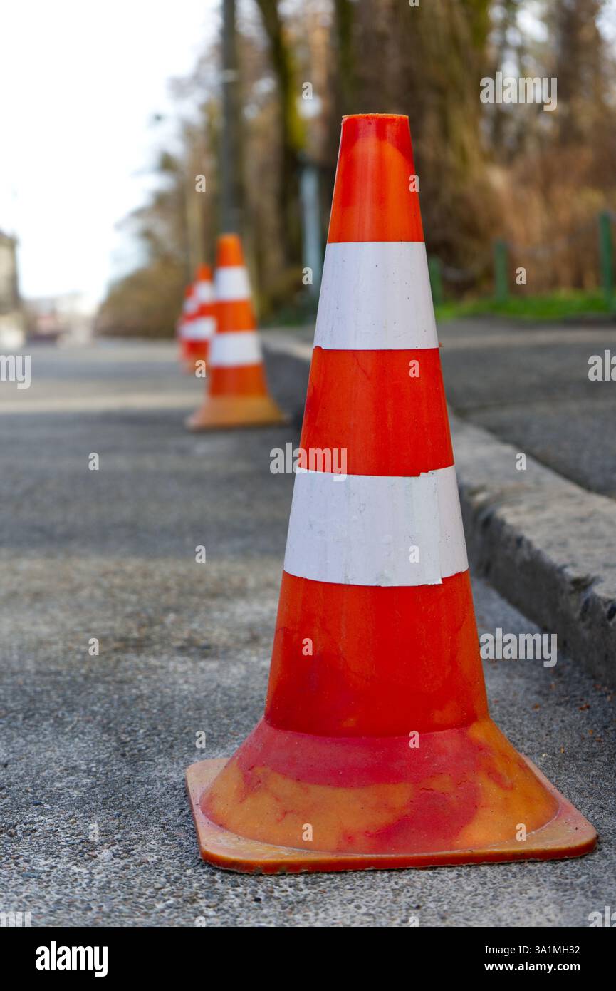 Une ligne de cônes orange vif se dresse sentinelle sur une rue asphaltée, marquant une limite ou une zone restreinte. Banque D'Images