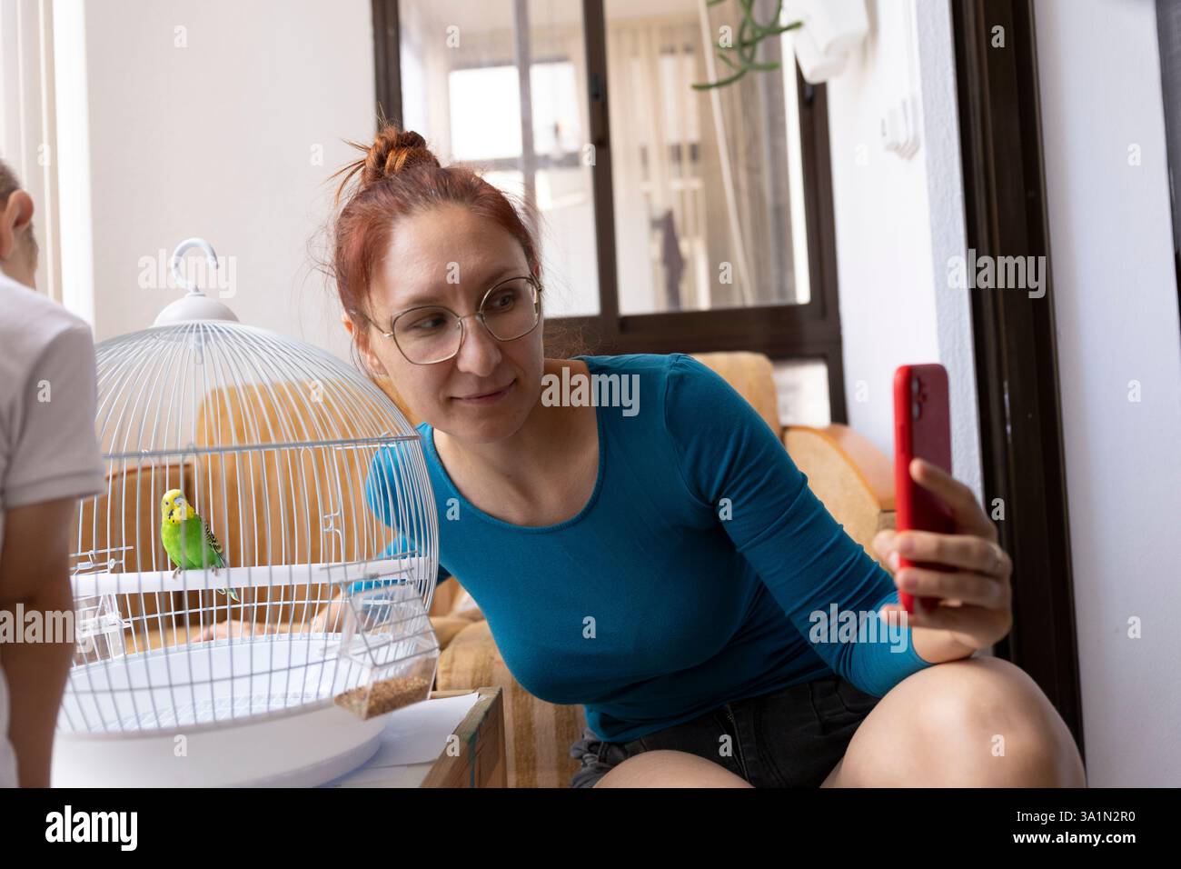Femme prenant des photos de perroquet en cage avec smartphone Banque D'Images