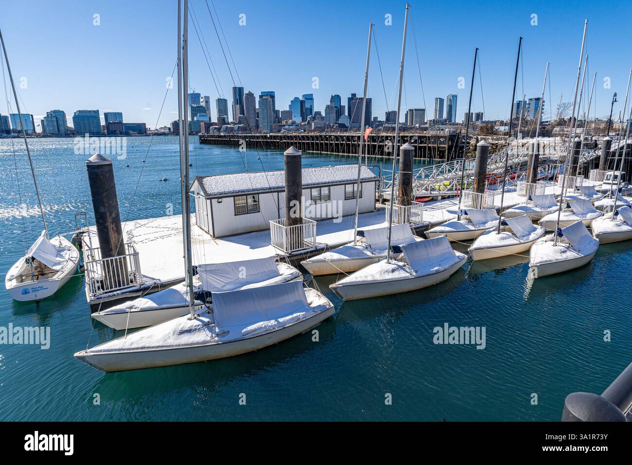 Boston, ma, États-Unis - 21 février 2025 - stationné de petits voiliers couverts de neige d'hiver à Piers Park à East Boston avec une ligne d'horizon lointaine de Boston dans le dos Banque D'Images