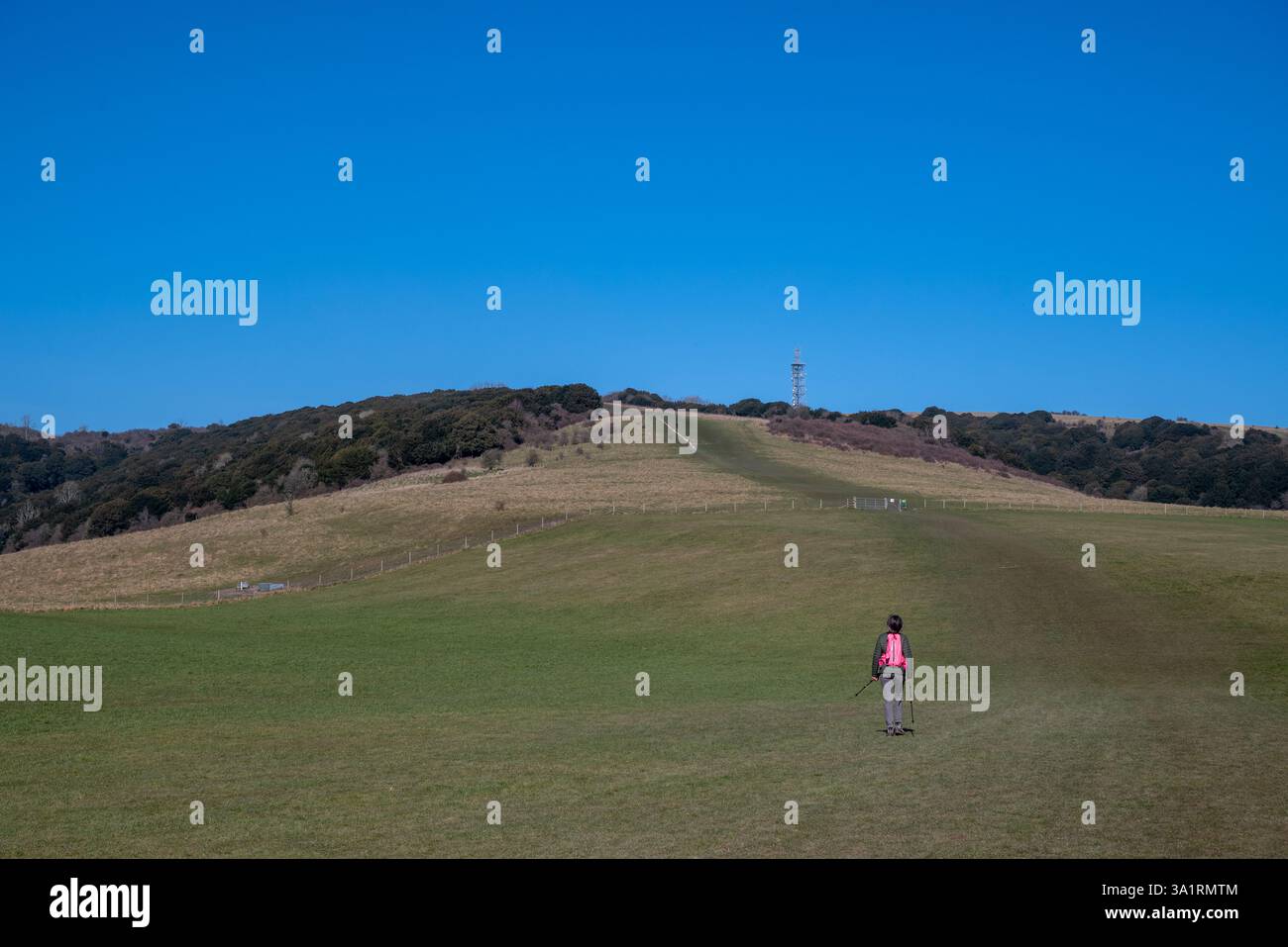 Une dame randonneuse commence la marche jusqu'à la colline Butser. Elle a des vêtements chauds, des bottes de randonnée et des bâtons de randonnée ainsi qu'un sac à dos rose vif. Mars 2025. Banque D'Images