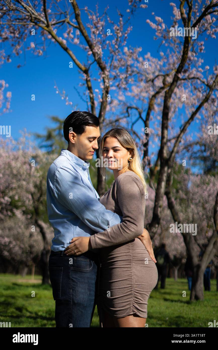 Heureux couple latin embrassant dans un beau verger fleuri, profitant de la journée ensoleillée de printemps Banque D'Images
