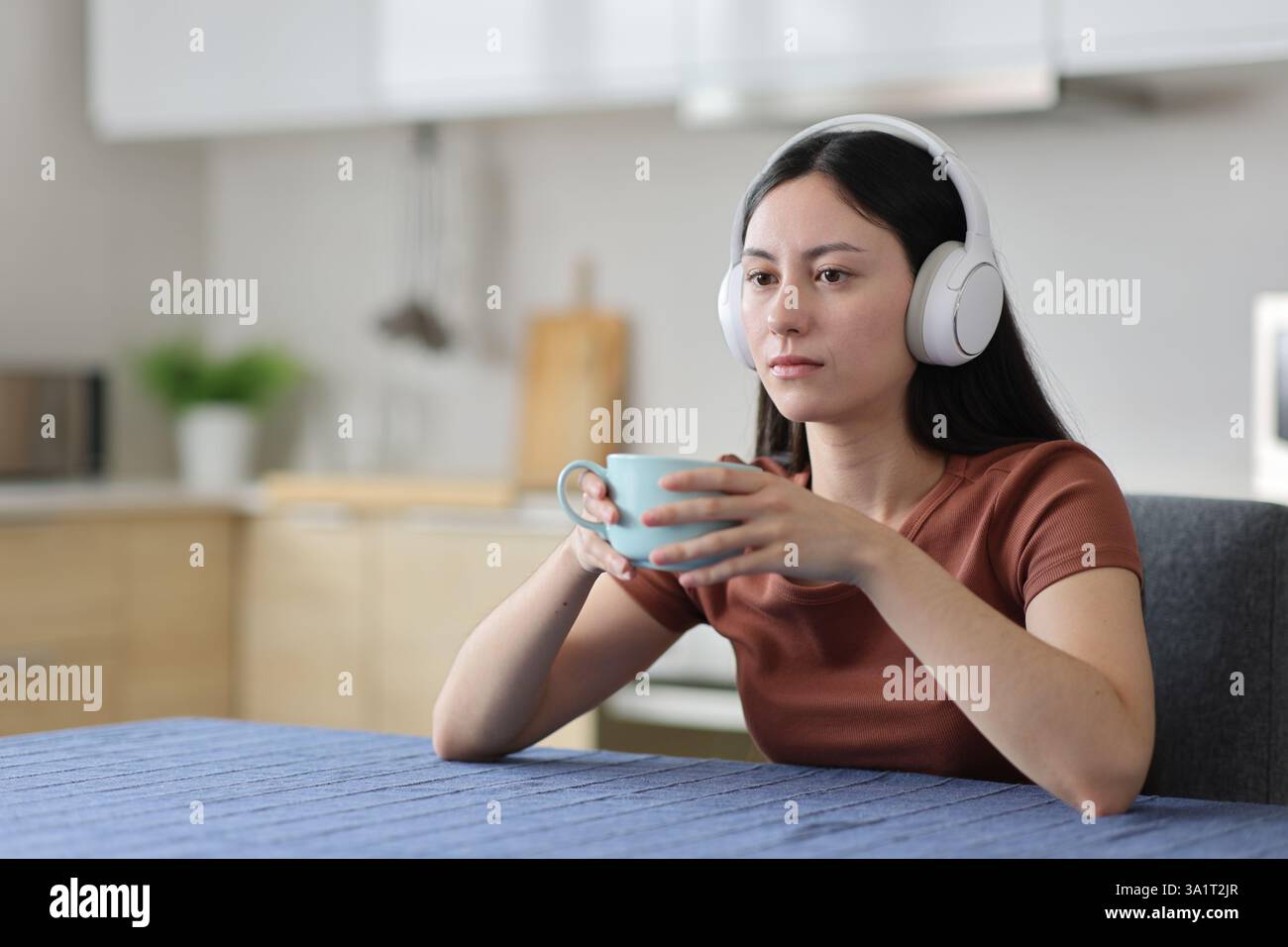 Femme asiatique dissimulée portant des écouteurs écoutant de la musique buvant du cofee dans la cuisine à la maison Banque D'Images