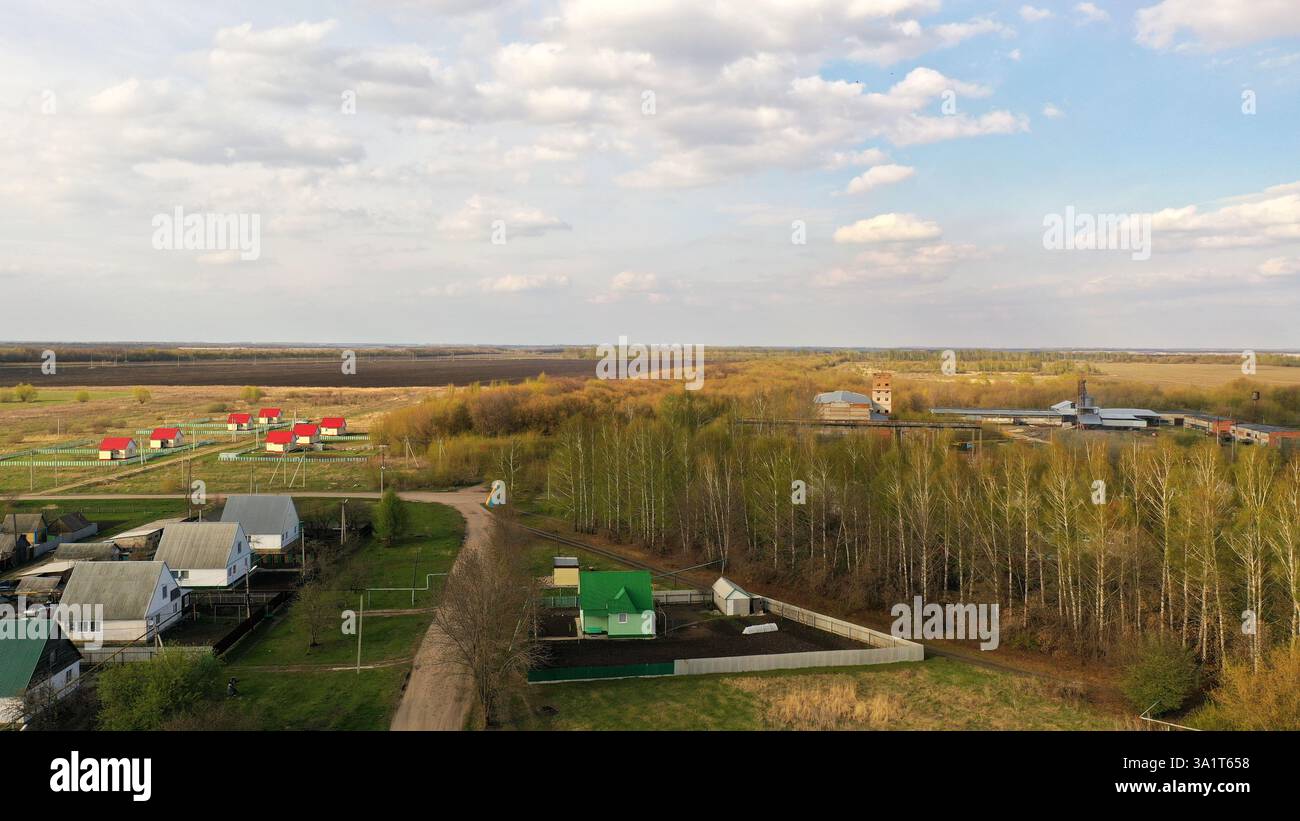 Paysage printanier montrant des maisons, une usine et une forêt, soulignant le mélange de la vie rurale et de l'industrie Banque D'Images