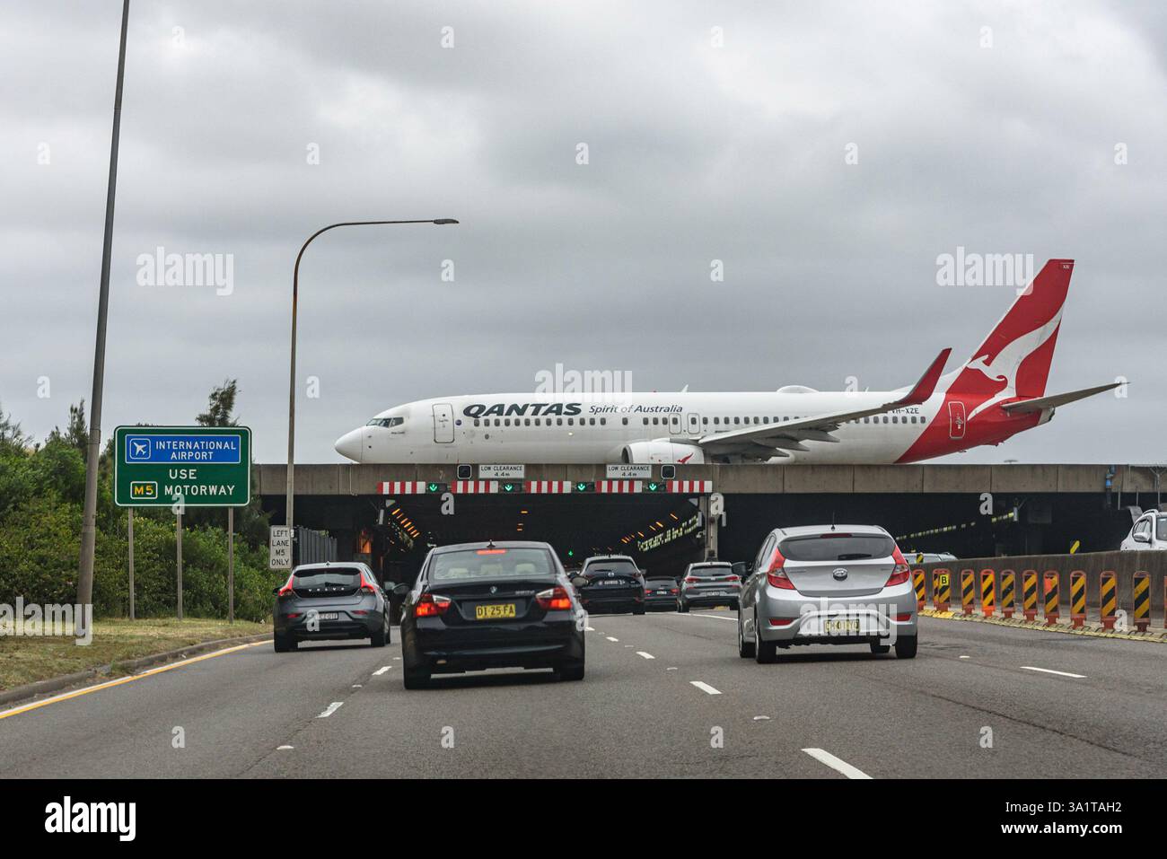 Un Boeing 737-800 de Qantas (VH-XZE) circulant sur la piste de l'aéroport de Sydney Kingsford Smith, qui passe au-dessus de l'autoroute M1/M5 Banque D'Images