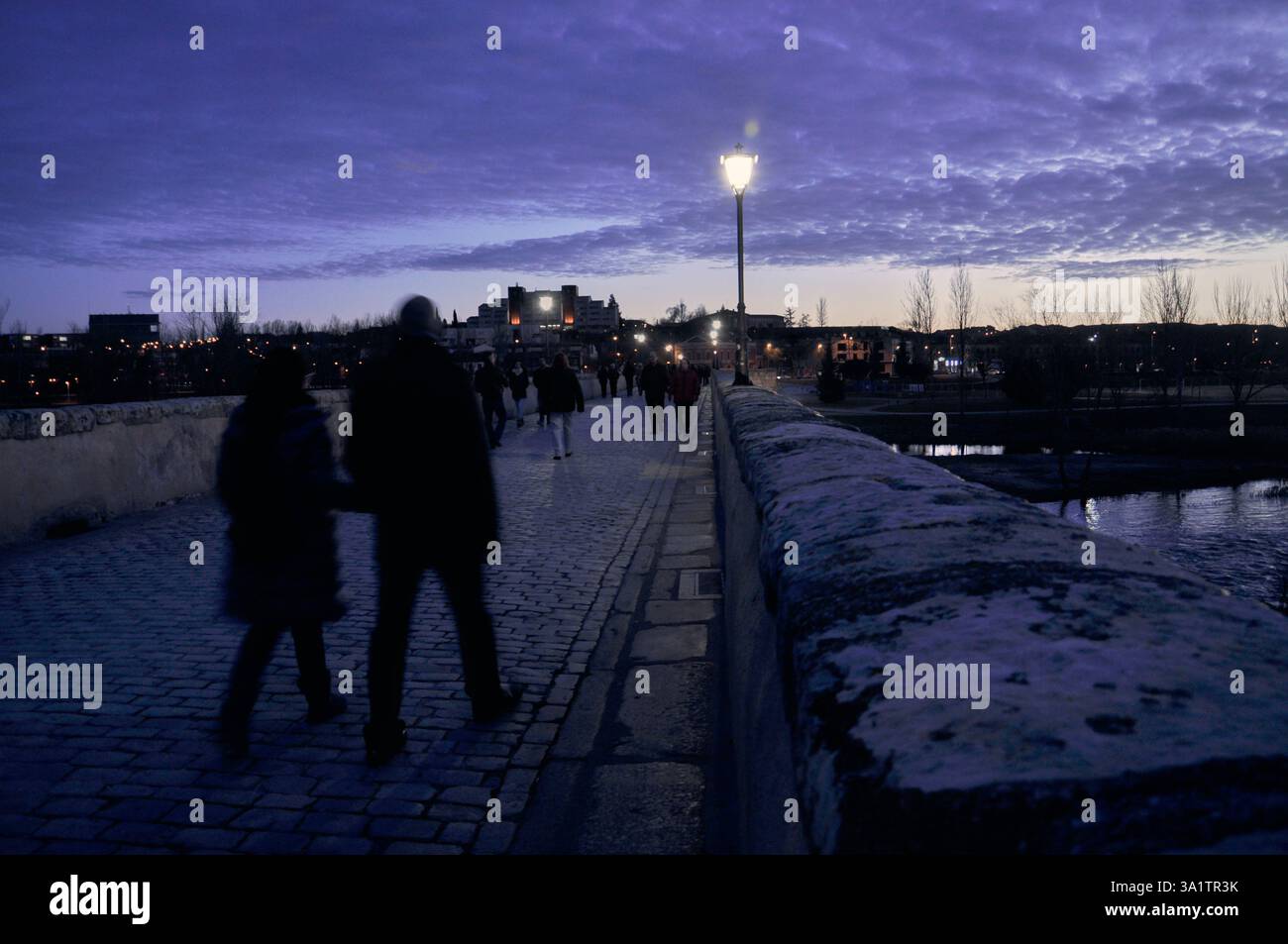 Les gens traversent le pont romain de Salamanque au coucher du soleil sous un magnifique ciel violet Banque D'Images