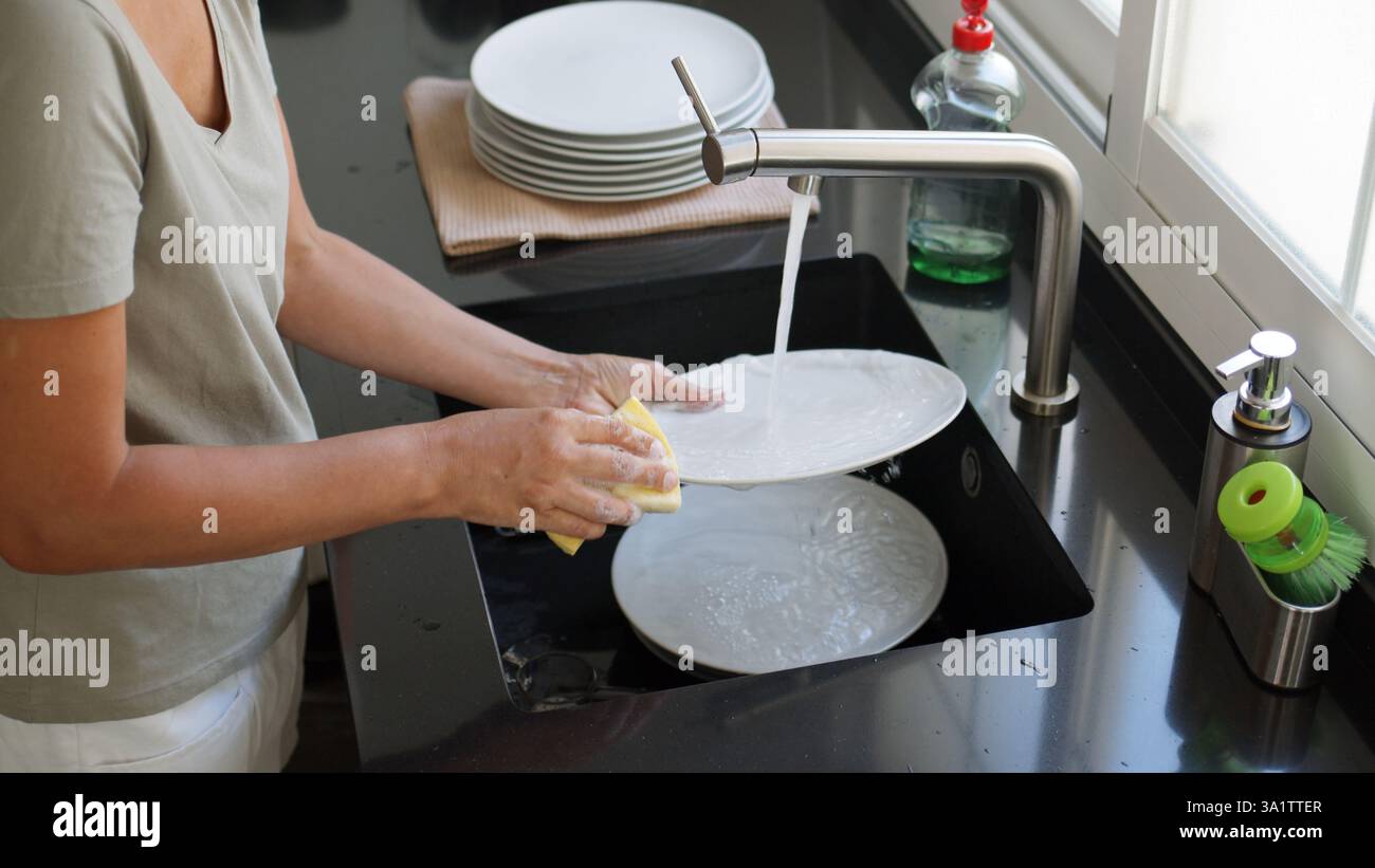Femme lavant et rinçant la vaisselle à la main sous un jet d'eau dans l'évier de la cuisine. Procédé de lavage de vaisselle. Banque D'Images