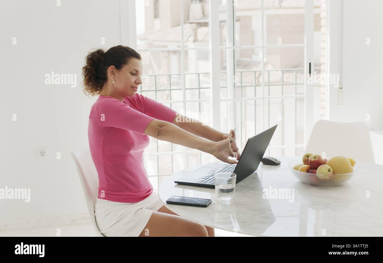 Femme d'âge moyen travaille sur un ordinateur à la maison, prend une pause de repos. Banque D'Images