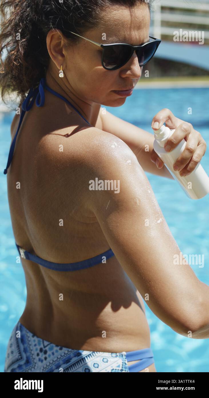 Femme appliquant un écran solaire ou un spray bronzant solaire à son épaule près de la piscine d'eau. Prendre soin de la peau et la protéger du soleil. Sain holid Banque D'Images