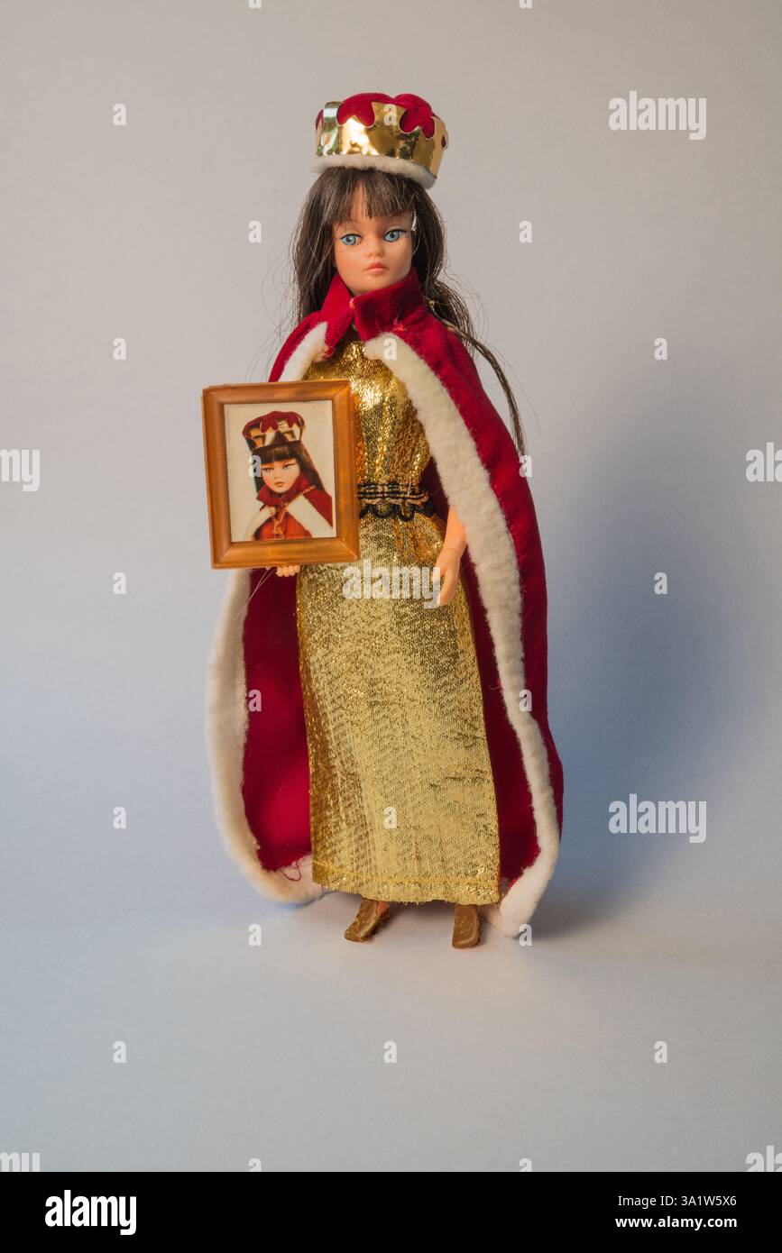 Poupée action Girl des années 1970 par Palitoy en tenue reine de beauté (robe dorée, cape rouge garnie de fourrure, couronne et photographie encadrée) Banque D'Images