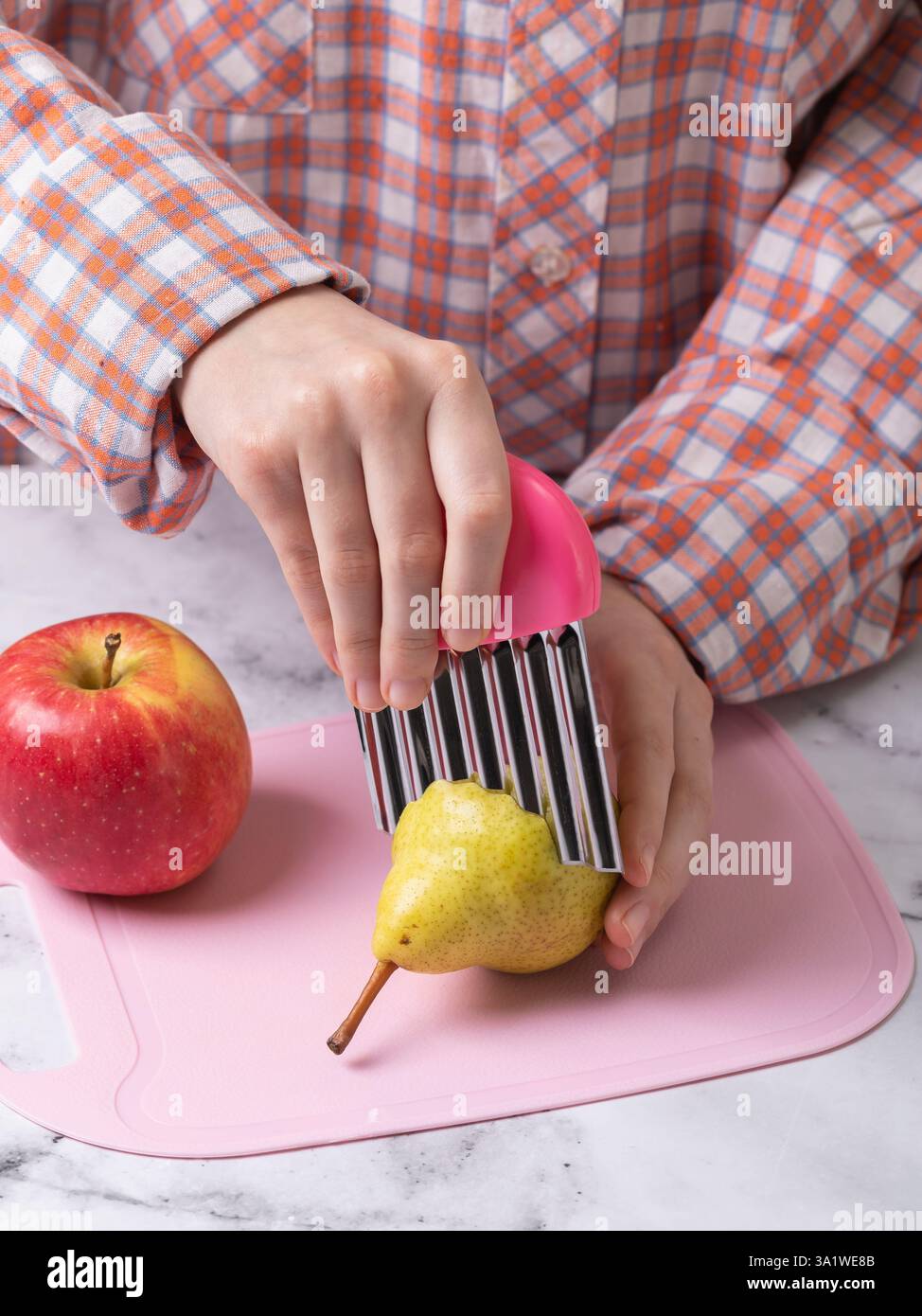 Enfant utilisant un couteau ondulé en acier inoxydable coupant la poire sur le sanglier rose coupant Banque D'Images