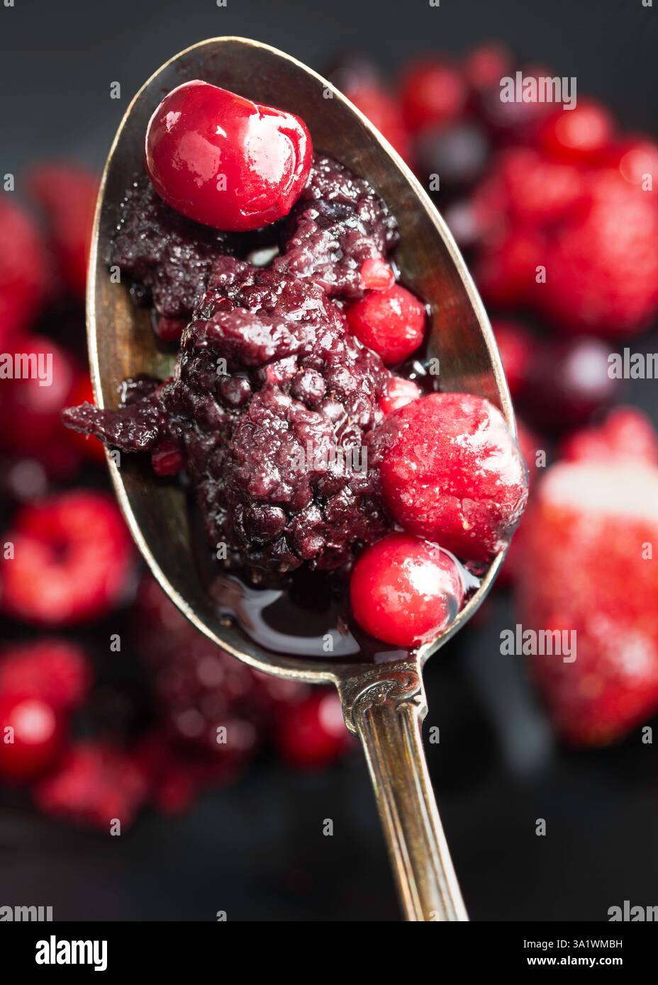 La photographie montre un gros plan d'une cuillère en métal remplie d'un mélange de baies, y compris des cerises, des mûres et des framboises. Banque D'Images