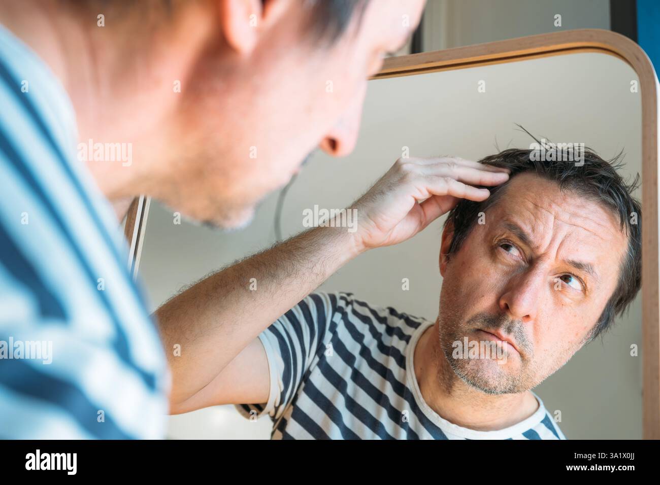 Concept de perte de cheveux, homme adulte adulte inquiet regardant miroir à sa ligne de cheveux du front, mise au point sélective Banque D'Images