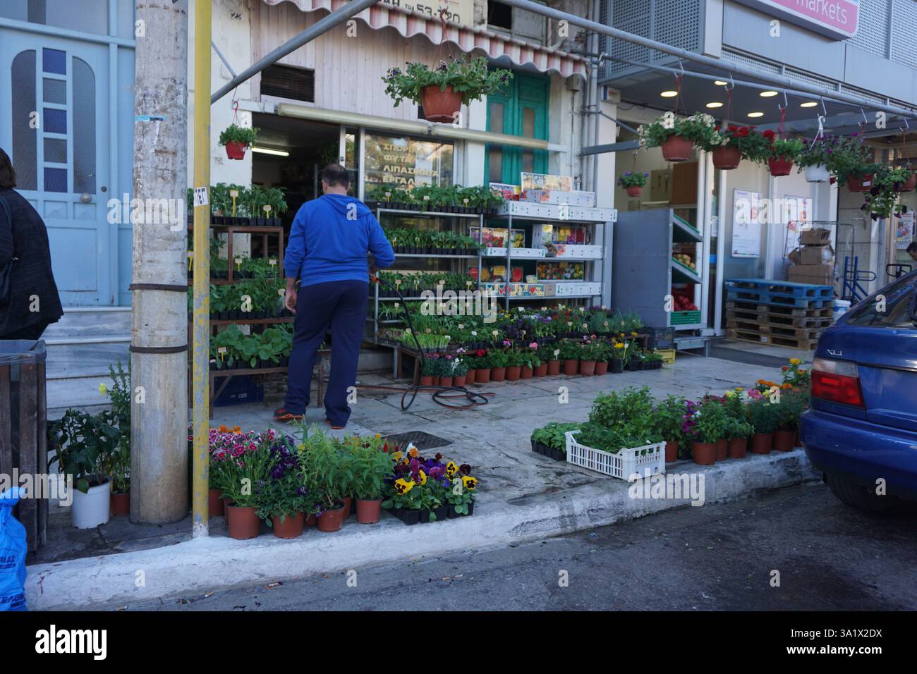 Un homme tient un tuyau et arrose les fleurs et les plantes dans des pots qu'il a placés sur le trottoir à l'extérieur de son magasin Banque D'Images