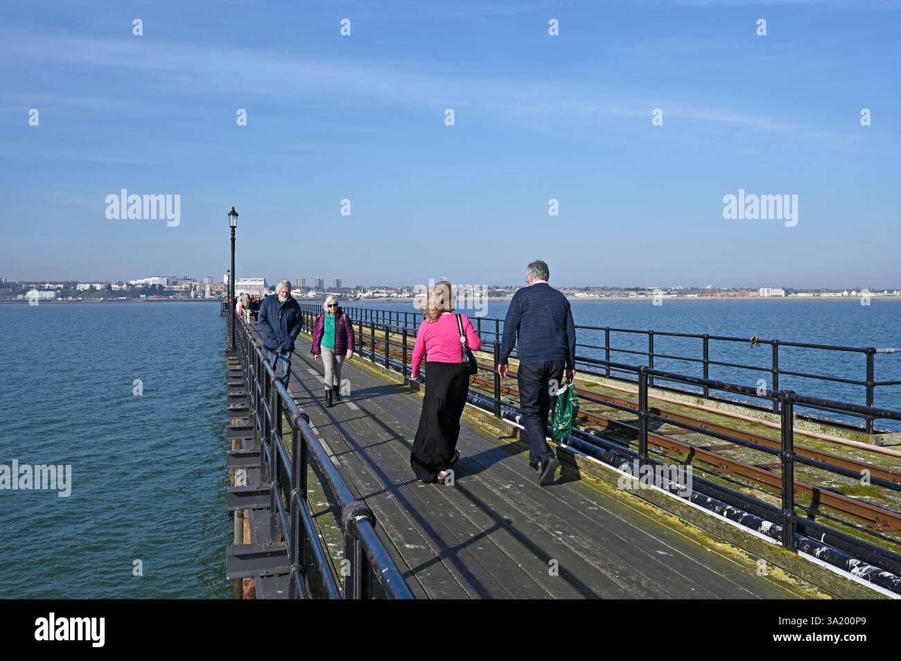 Au premier plan, un couple marche vers le rivage et un autre couple marche vers le Pier Head sur la plus longue jetée de plaisir du monde. Southend. ROYAUME-UNI Banque D'Images