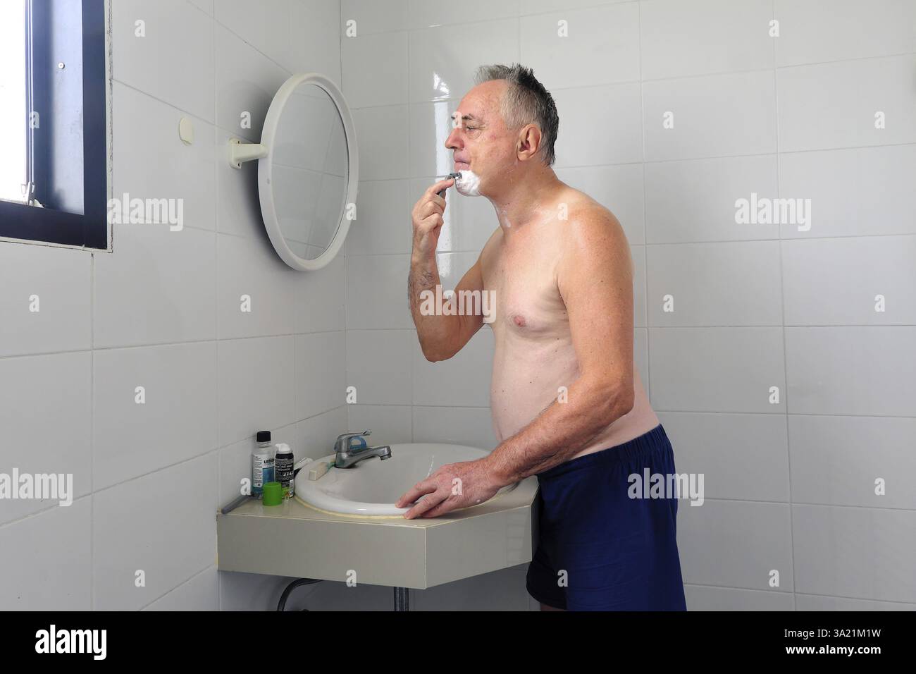 Man 60 plus se rase mouillé dans la salle de bain Banque D'Images