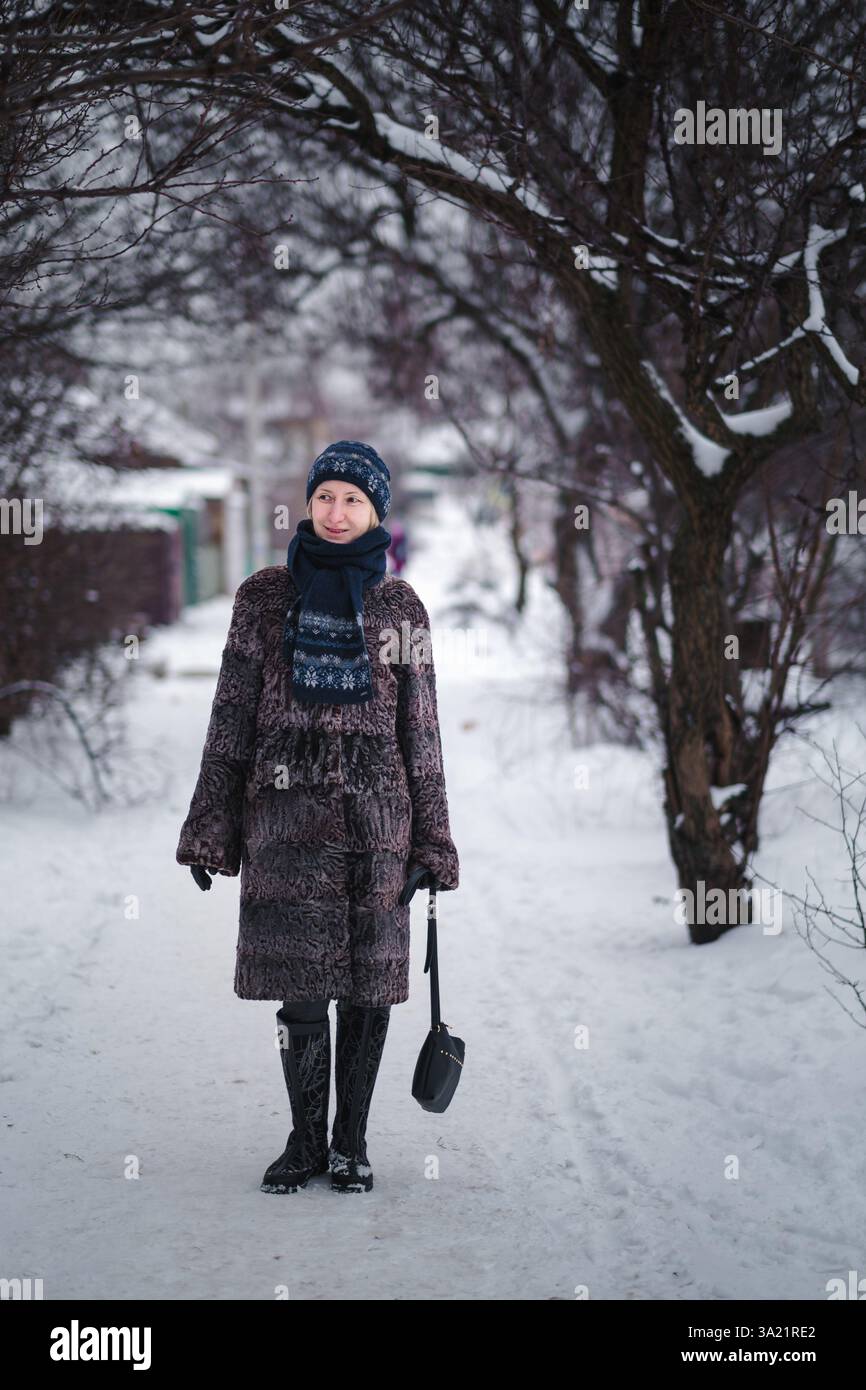 Une femme en manteau de fourrure karakul marche le long d'un chemin enneigé, entourée de profondes déneigements qui couvrent tout ce qui est en vue. Banque D'Images
