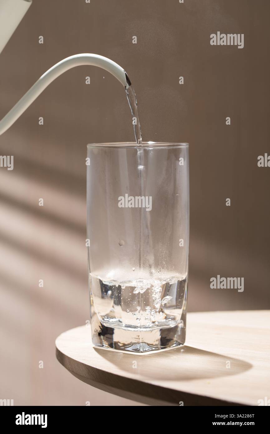 Une bouilloire verse de l'eau chaude dans un verre, la vapeur s'élevant lorsque l'eau remplit le verre, capturant l'interaction entre l'eau chaude et le verre froid Banque D'Images