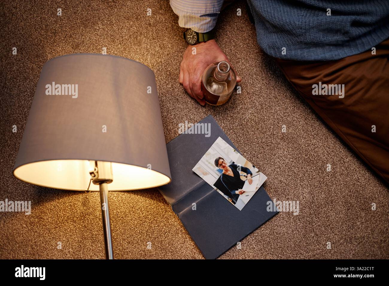 Personne assise sur le sol de moquette tenant la boisson tout en lisant le document sous la lumière chaude de la lampe, créant une atmosphère paisible et concentrée Banque D'Images