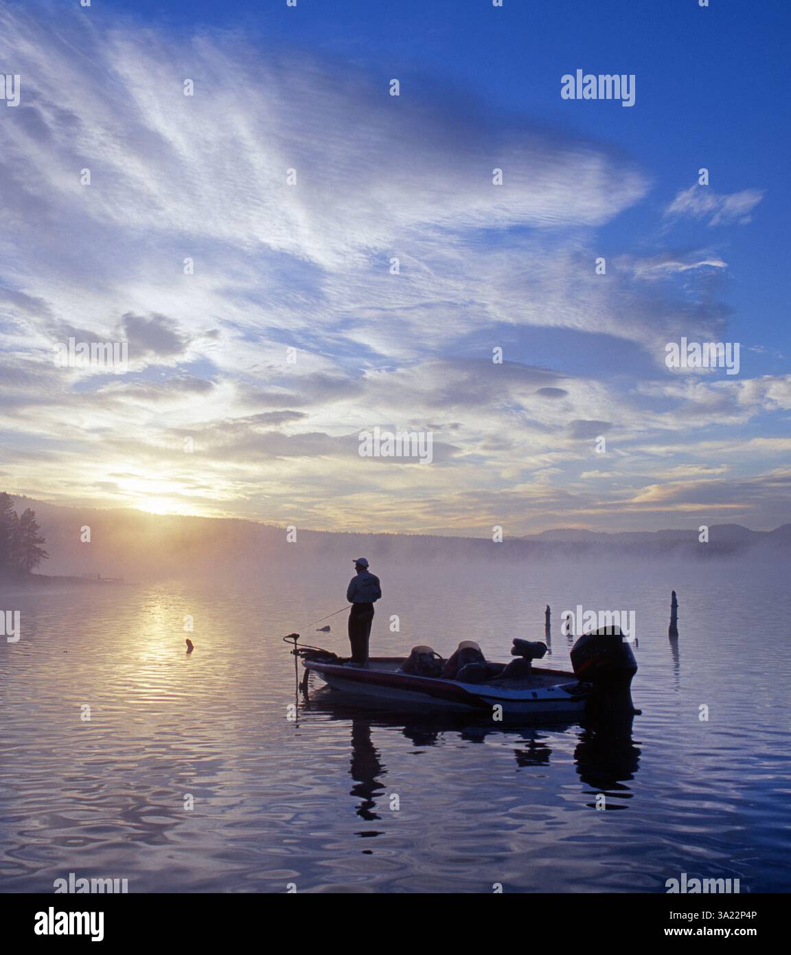 Un pêcheur de bar jette le bar à grande bouche à l'aube sur une montagne brumeuse d'été sur un lac de montagne dans les montagnes Oregon Cascade. Banque D'Images